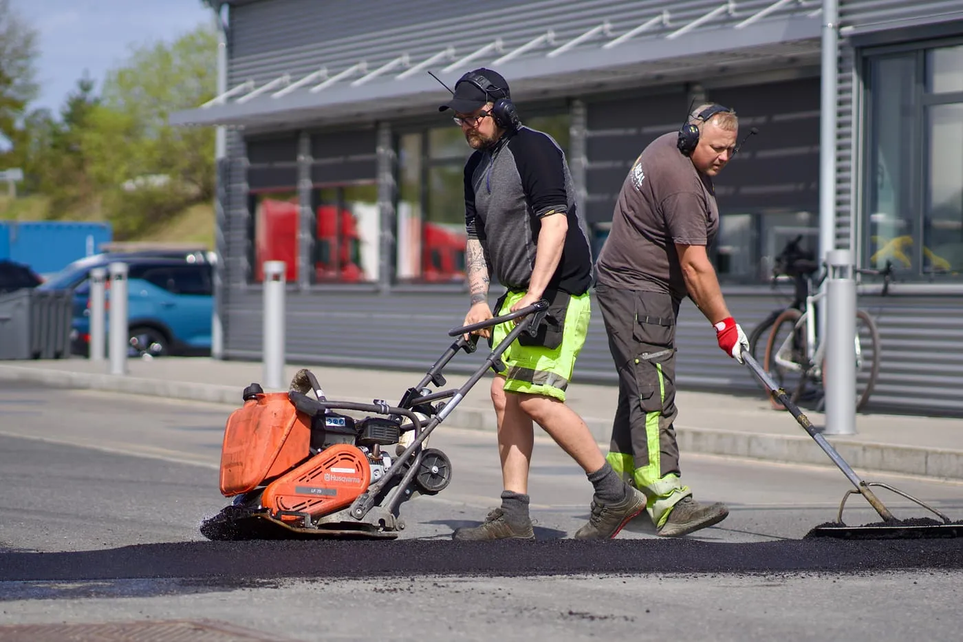 To asfaltarbeidere jobber med plate og rake på et nytt dekke
