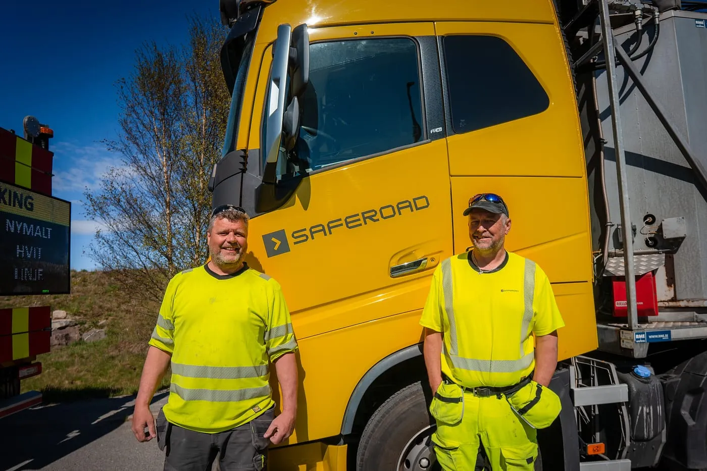 To arbeidere foran en lastebil merket Saferoad